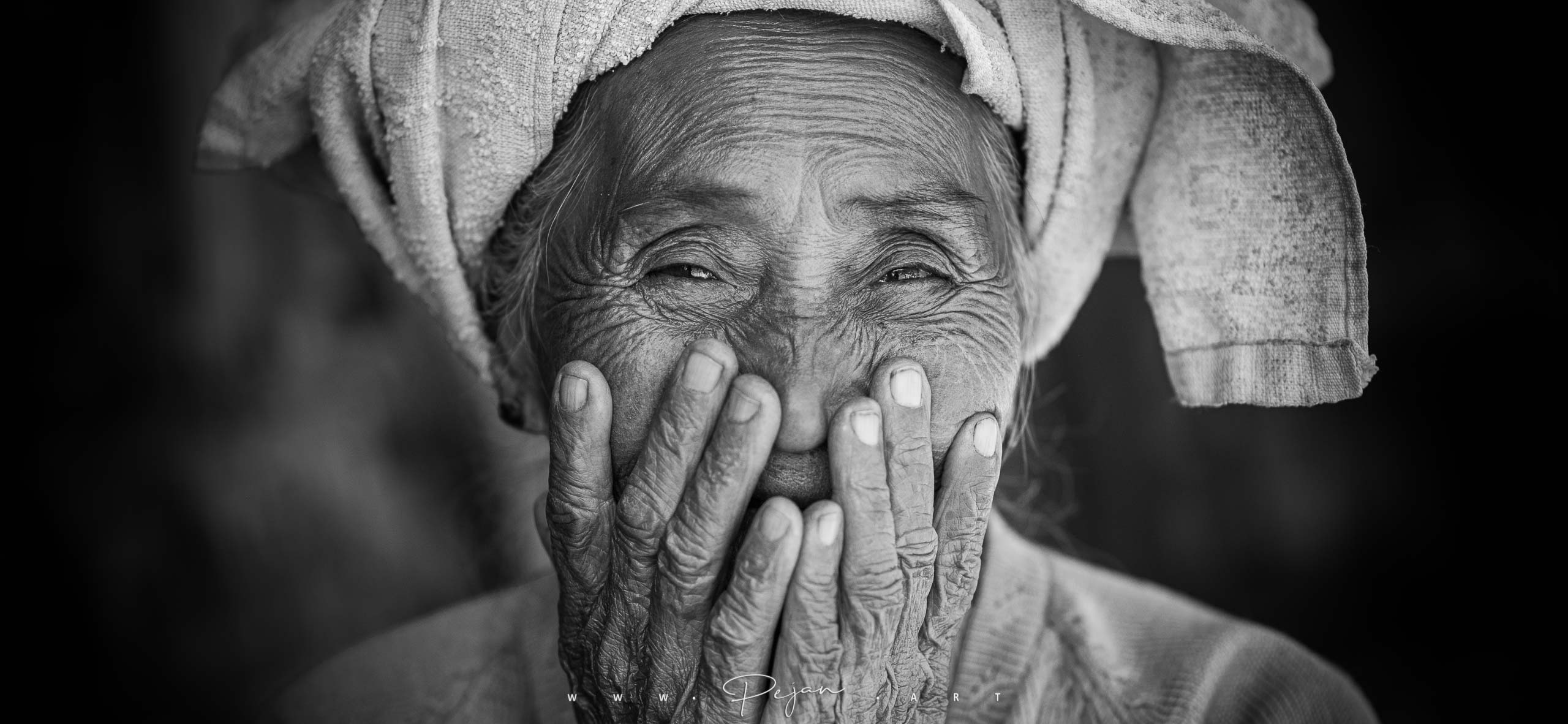 Monochrome portrait of a beautiful elderly woman in the mountains of Shan State, Myanmar. She covers her mouth with her hands out of modesty. She wears the traditional towel of the ethnic groups of this region.