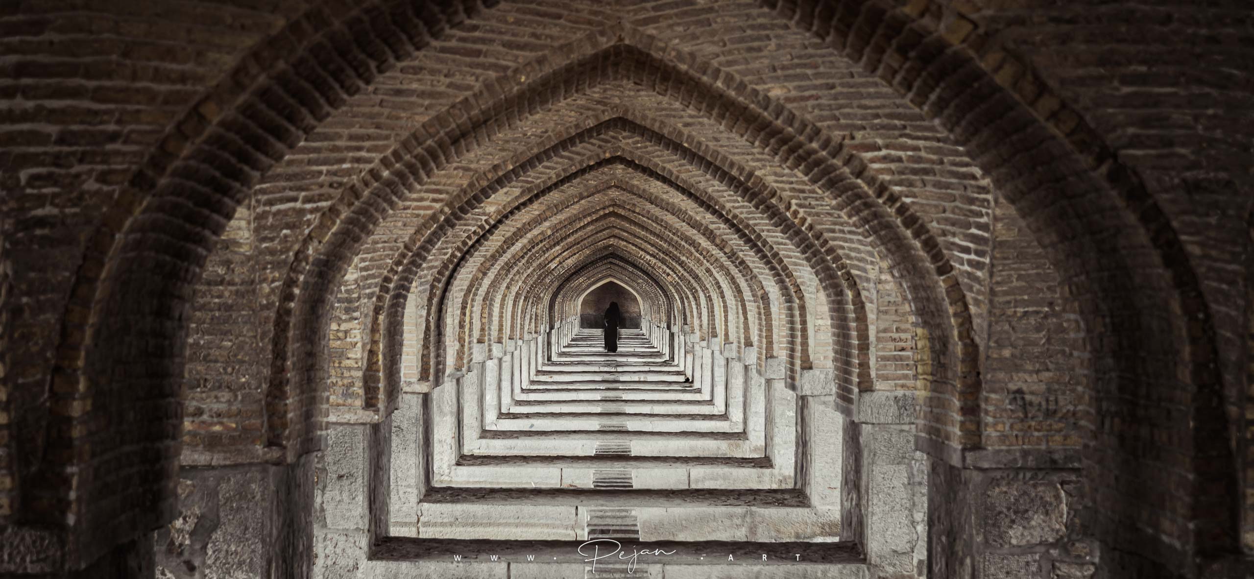 A woman wearing chador walks under the Khaju Bridge in Isfahan, Iran. Iconic image. Iranian architecture. Door tunnel. Perspective with vanishing point. repetition.