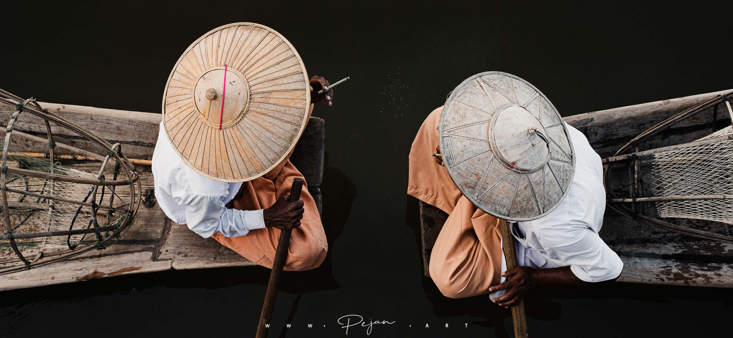 Deux pêcheurs de l'ethnie Intha fume un cheroot, Ils sont assis face à face sur leur barques sur le lac Inle et ils portent des chapeaux traditionnels asiatiques, État Shan, Birmanie