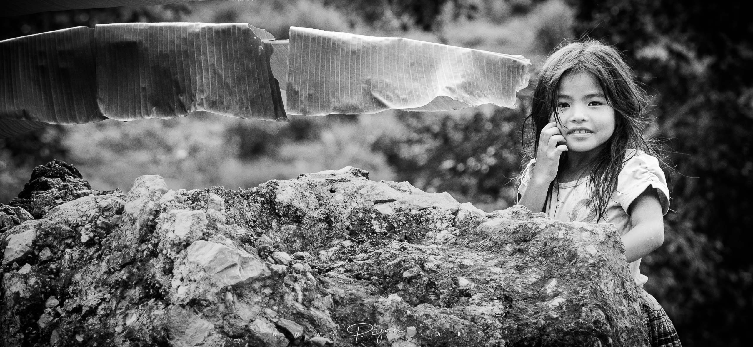 Photographie noir et blanc, une jeune fille au cheveux long dans la campagne du Nord du Vietnam, elle regarde l'objectif.