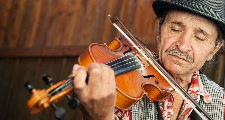 Travel diaries in Eastern Europe - Portrait of a Gypsy violinist in Rosia Montana in the Apuseni Mountains, Romania. The man wears a traditional hat and plays the violin. With his eyes closed, he seems carried away by the music.