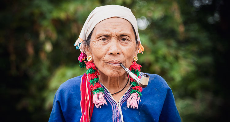 Portrait d'une femme de l'ethnie Karen rencontrée dans les montagnes en Thaïlande. Elle porte des vêtements et bijoux traditionnels et fume une grande pipe. Elle regarde l'objectif.