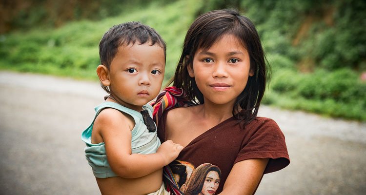 Portrait of a young girl holding her little brother in her arms in the mountains of northern Laos, cycling trip in Asia