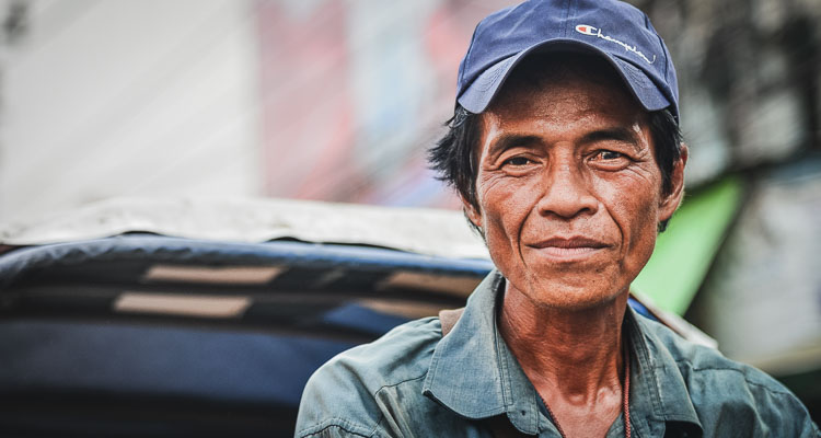 Street Portrait, Tuk Tuk driver in Bangkok, Thailand. The man smiles and looks at the camera. He wears a blue cap and shirt