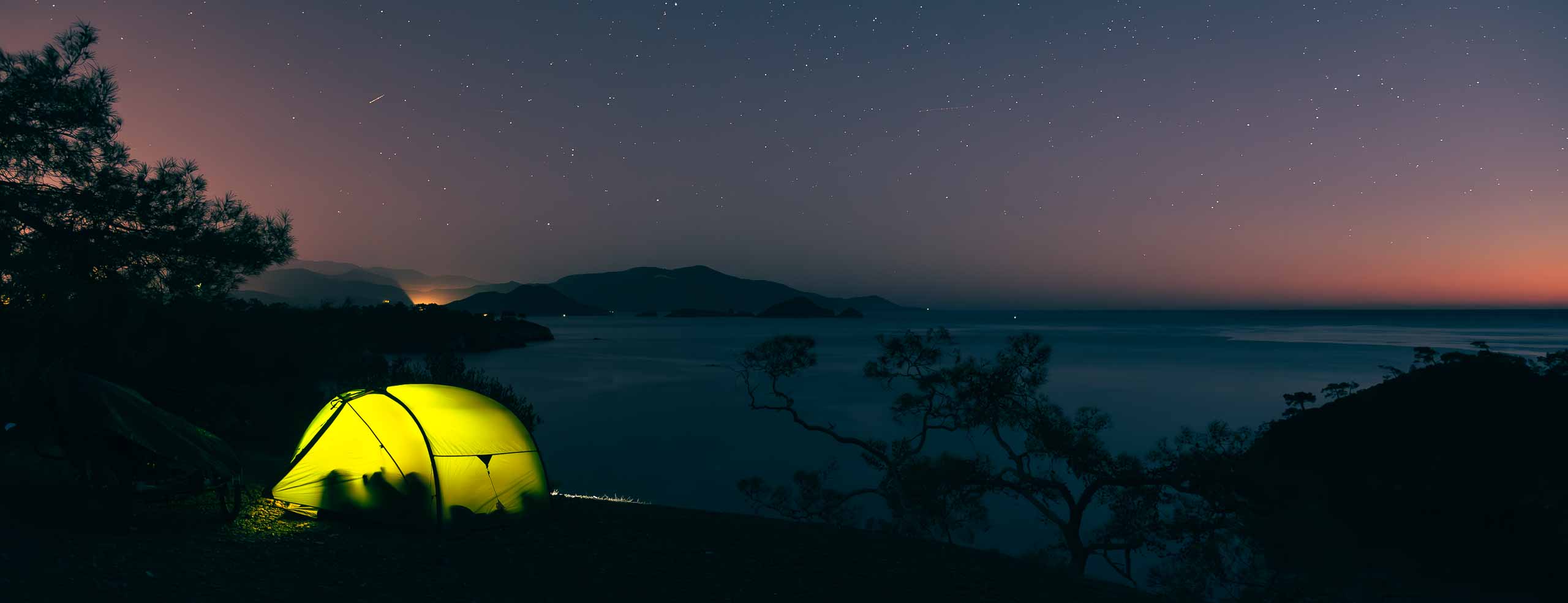 Tente Exped Venus II illuminée de nuit sur une falaise surplombant la mer Égée, bivouac sous un ciel constellé d'étoiles près de Fethiye, Turquie