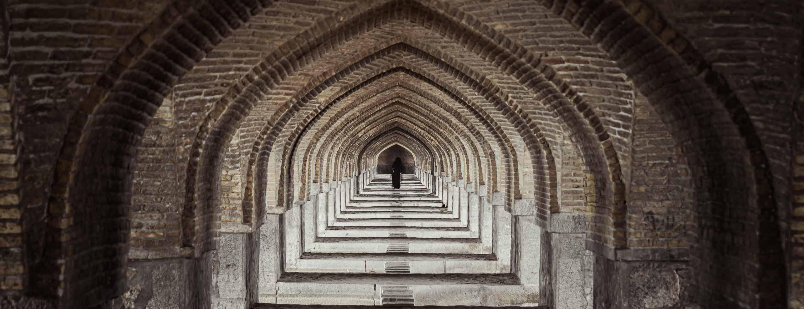 Une femme portant le chador marche sous le pont Khaju à Ispahan, en Iran. Image iconique. architecture iranienne. Tunnel de portes. Perspective avec point de fuite. répétition.