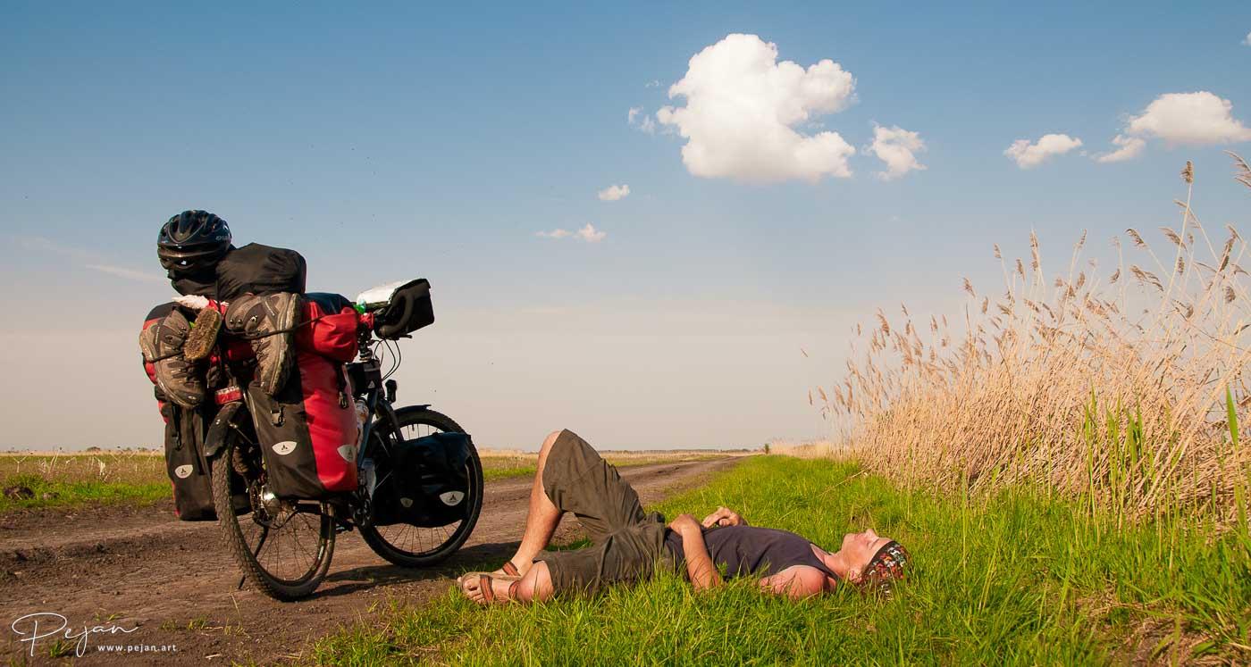 Voyageur allongé dans l'herbe au soleil, à côté d'un vélo de voyage chargé, cyclotourisme, aventure, tour du monde, Hongrie