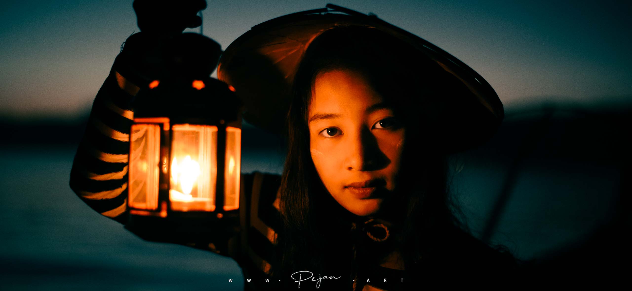 Portrait d'une jeune fille de l'ethnie Intha qui tient une lampe. La photo est prise de nuit et la lumière se reflète sur son visage. Lac Inle, Birmanie